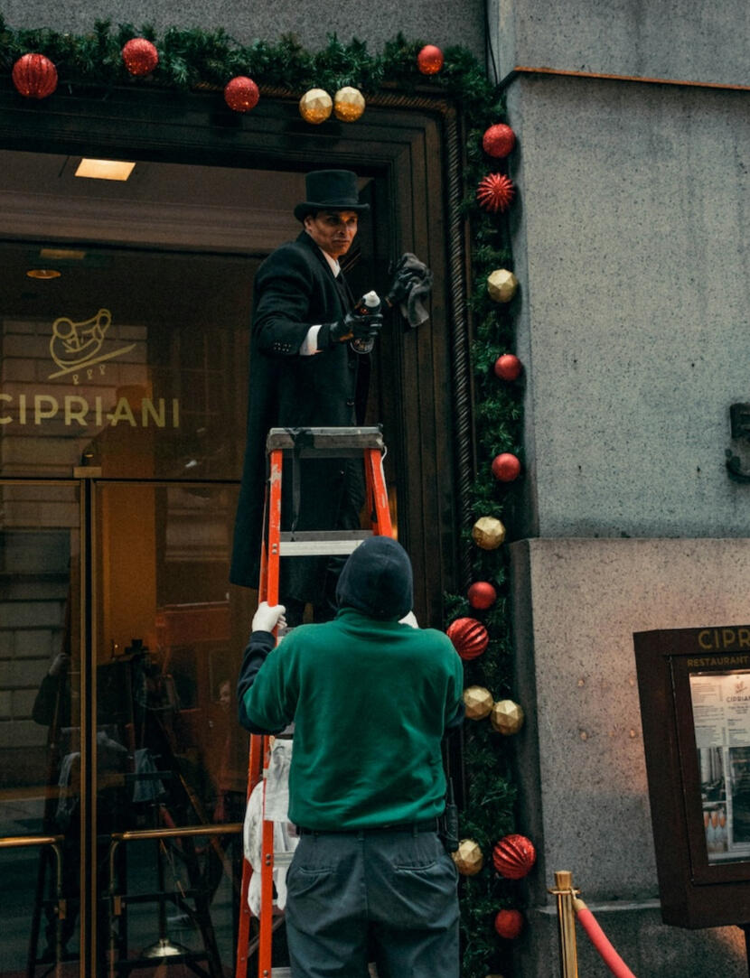 A Cipriani doorman wearing a traditional top hat and coat arranging elegant holiday decorations outside the luxury venue in New York City.