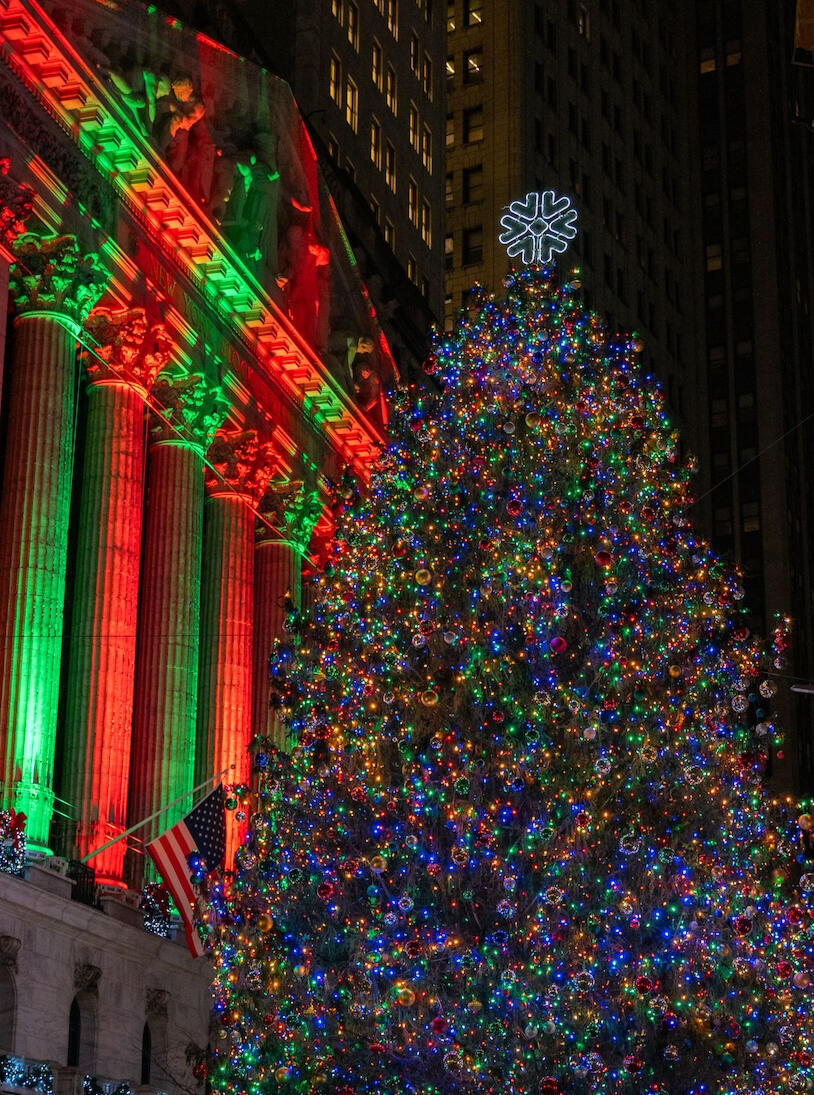 The massive decorated Christmas tree lit up at night in front of the New York Stock Exchange building on Wall Street.